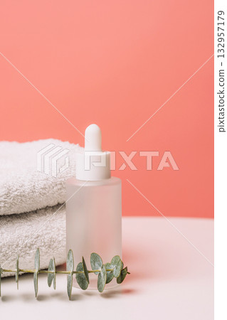 Vertical cosmetic dropper bottle with towel and eucalyptus on pink Vertical cosmetic dropper bottle with towel and eucalyptus on pink 132957179
