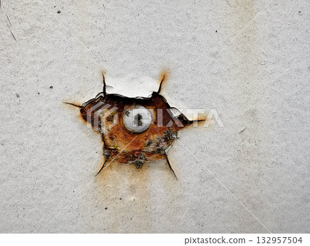 Aged metal texture. A rusty nail protrudes from beneath cracked white paint on a rusty metal surface. Aged metal texture. A rusty nail protrudes from beneath cracked white paint on a rusty metal surface. 132957504