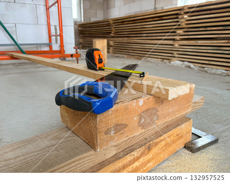 A tape measure, pencil, and handsaw lie on a board. Construction tools and measuring instruments. A tape measure, pencil, and handsaw lie on a board. Construction tools and measuring instruments. 132957525
