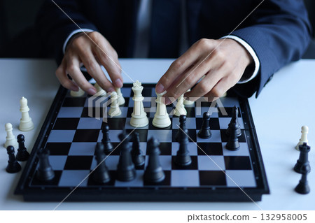 Businessman wearing suit, playing chess, game of strategy, leadership and management concept. 132958005