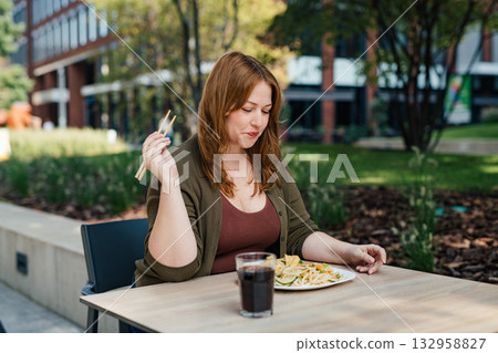 Plus size woman having lunch outdoors, eating noodles. 132958827