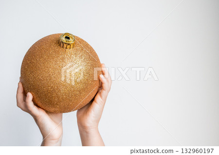 Child hands holding large golden Christmas ornament against white background Child hands holding large golden Christmas ornament against white background 132960197