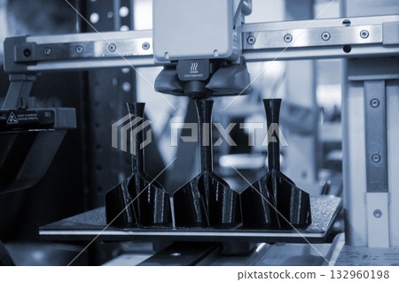 Shank stabilizer printing on 3D printer from molten plastic on desktop of 3d printer. Plastic stabilization tail creating on 3D printer. Black prototype model of rocket bomb tip printing on 3D printer 132960198
