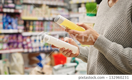 Woman comparing dog or cat shampoo in pet store. Responsible pet owner choosing pet care products. Customer reading the label and checking ingredients before purchase, choosing pet grooming product. 132960231