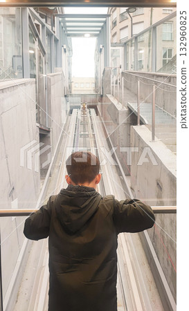 A toddler boy looks at the elevator mechanism in a transparent cable car. Concept of modern technology, child development 132960825