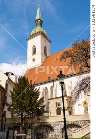 St. Martin's Cathedral stands prominently against the Bratislava skyline, showcasing its historical architecture. Nearby buildings and a clear sky add to the urban landscape's charm 132961174