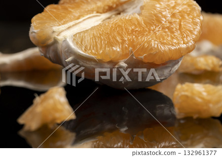 half of an orange citrus on a mirror surface, ripe sweet and juicy citrus is reflected on the black surface 132961377