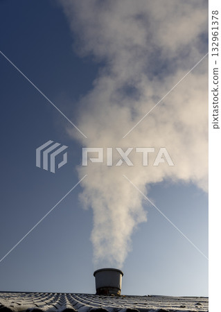 white smoke coming from a wide pipe against a blue sky background, white steam coming from a pipe during heating of a large industrial premises in cold weather 132961378
