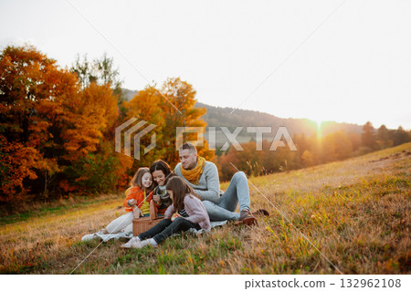 Parents with young children sitting outdoors in autumn light. Parents with young children sitting outdoors in autumn light. 132962108