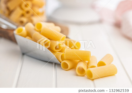 Uncooked rigatoni pasta in scoop on white table. Uncooked rigatoni pasta in scoop on white table. 132962539
