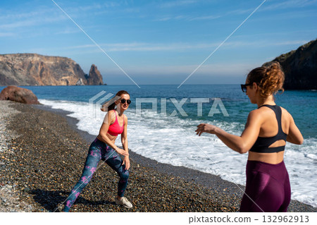 Fitness women stretching routine on pebble beach by scenic sea cliffs Fitness women stretching routine on pebble beach by scenic sea cliffs 132962913