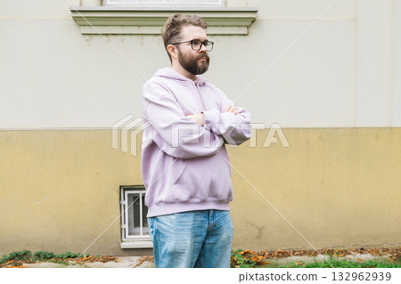 Sad man standing near building wall with folded arms. Copy space and empty place for advertising. Confidence, isolation, and personal reflection. 132962939