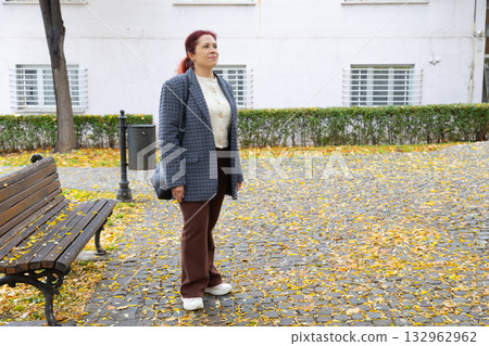Woman standing on street covered with fallen leaves. Copy space and empty place for advertising. Autumn nostalgia, quiet reflection, and gentle solitude in city life. Woman standing on street covered with fallen leaves. Copy space and empty place for advertising. Autumn nostalgia, quiet reflection, and gentle solitude in city life. 132962962