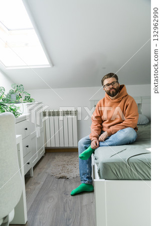 Man sitting on bed with thoughtful expression. Representation of introspection, emotional awareness and daily simplicity in private home interior. 132962990
