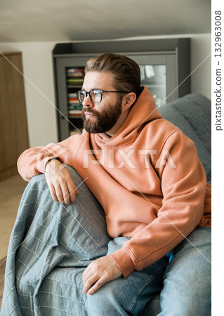 Man sitting on couch with thoughtful expression. Concept of introspection, solitude, daily routine and mental focus in cozy domestic atmosphere. Man sitting on couch with thoughtful expression. Concept of introspection, solitude, daily routine and mental focus in cozy domestic atmosphere. 132963008