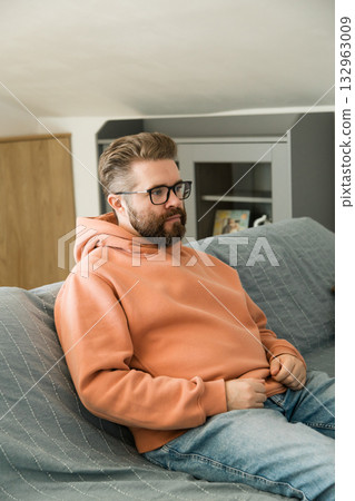 Man sitting on sofa and looking ahead. Moment of stillness symbolizing contemplation, patience, inner focus and everyday thinking at home interior. Man sitting on sofa and looking ahead. Moment of stillness symbolizing contemplation, patience, inner focus and everyday thinking at home interior. 132963009