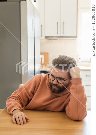 Man leaning on table with thoughtful expression. Symbol of fatigue, burnout, reflection and emotional pause during remote work or daily digital activity. 132963016