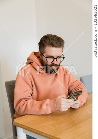 Man using smartphone while sitting at desk. Everyday activity reflecting digital communication, concentration, technology dependence and social media interaction in contemporary lifestyle. Man using smartphone while sitting at desk. Everyday activity reflecting digital communication, concentration, technology dependence and social media interaction in contemporary lifestyle. 132963023