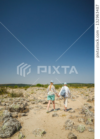 Two women walking hand in hand through the stone desert of Pobiti Kamani near Varna, Bulgaria, under a clear blue sky. 132963487