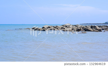 Rocky Breakwater on a Tropical Seashore Against a Bright Blue Sky and Calm Blue Ocean Water Rocky Breakwater on a Tropical Seashore Against a Bright Blue Sky and Calm Blue Ocean Water 132964619