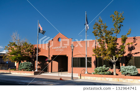 The red brick facade of Carson City City Hall in Nevada. An American flag and a Nevada state flag fly in front of the building under a clear blue sky. Represents local government and civic services The red brick facade of Carson City City Hall in Nevada. An American flag and a Nevada state flag fly in front of the building under a clear blue sky. Represents local government and civic services 132964741