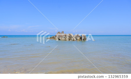 Isolated Jagged Rock Formation Floating in the Calm Ocean Water on a Bright, Clear Tropical Day 132965359