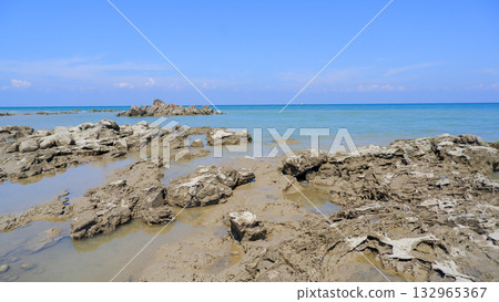 Tidal Rock Platform in Foreground Facing Distant Jagged Rock Outcropping in Calm Tropical Ocean 132965367