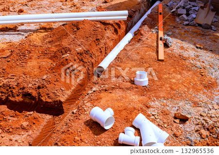 Workers are preparing construction site with freshly dug soil white plumbing pipes laid out for installation. Workers are preparing construction site with freshly dug soil white plumbing pipes laid out for installation. 132965536