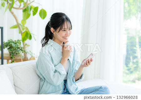 在房間裡操作智慧型手機的年輕女子 在房間裡操作智慧型手機的年輕女子 132966028