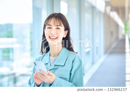 A woman in work clothes operating a smartphone with a smile A woman in work clothes operating a smartphone with a smile 132966237
