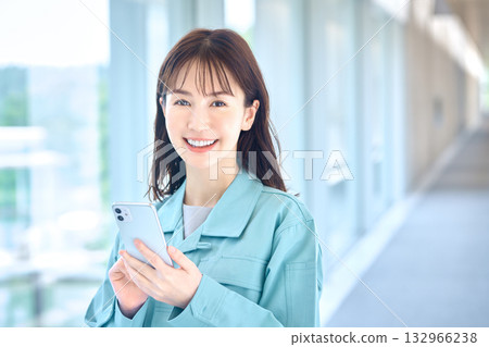 A woman in work clothes operating a smartphone with a smile A woman in work clothes operating a smartphone with a smile 132966238