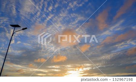 Vivid Altocumulus and Cirrus Clouds in Orange and Blue Sunset Sky with Silhouetted Solar Powered 132967198