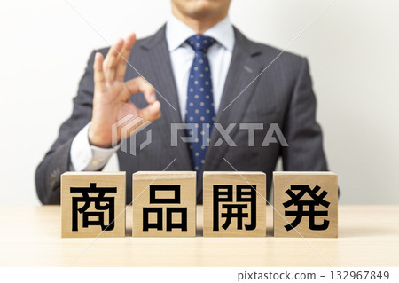 一位商人擺出「OK」的姿勢,旁邊立著一塊寫著「產品開發」的積木。 一位商人擺出「OK」的姿勢,旁邊立著一塊寫著「產品開發」的積木。 132967849