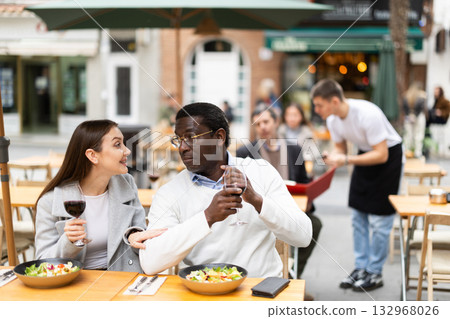 Interethnic couple happily chatting while sitting on the terrace of a restaurant 132968026