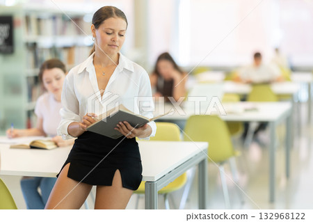 Young female student reading book in library Young female student reading book in library 132968122