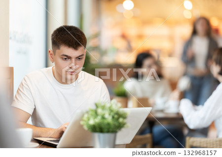 Young man sitting in cafe and working on laptop Young man sitting in cafe and working on laptop 132968157