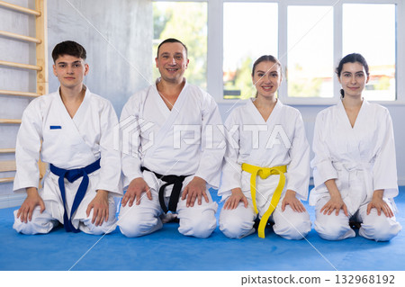 Young judo practitioners and middle-aged trainer sitting in seiza pose 132968192