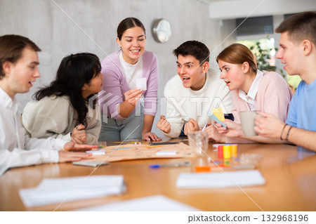 Carefree girl playing board game with friends at table Carefree girl playing board game with friends at table 132968196