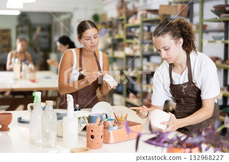 Girl and man processing clay bowls in carpentry workshop 132968227