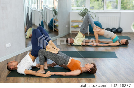 Happy couple doing stretching exercise during group acroyoga classes in gym Happy couple doing stretching exercise during group acroyoga classes in gym 132968277