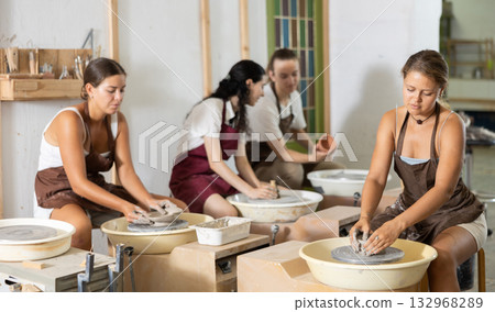 Young woman sits near potter wheel and makes clay crafts 132968289