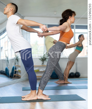 Lovers of active lifestyle perform pair yoga backbend balance pose in gym Lovers of active lifestyle perform pair yoga backbend balance pose in gym 132968293