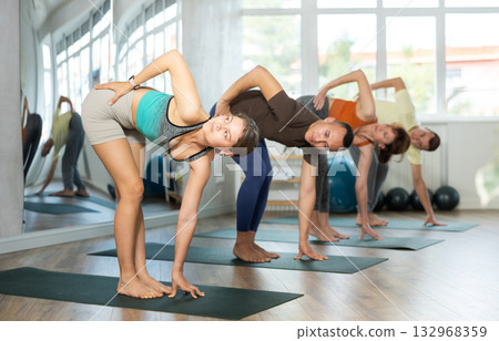 Women and men practicing downward dog pose of yoga during fitness classes 132968359