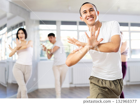 Positive young men and girls dancing modern street dance together during their group training at dance hall 132968377