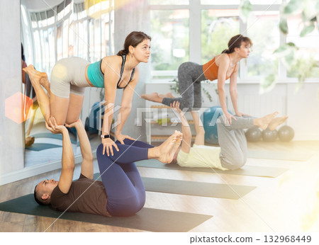 Multiethnic group of sporty people practicing various partner yoga positions during training in fitness gym, couple acro yoga 132968449