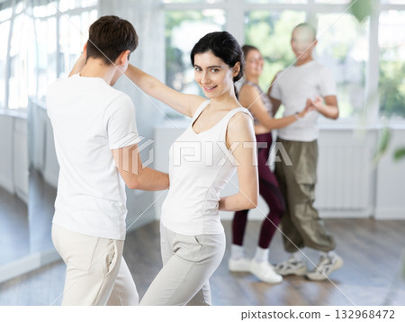 Cheerful young couple practicing passionate samba in dance class Cheerful young couple practicing passionate samba in dance class 132968472