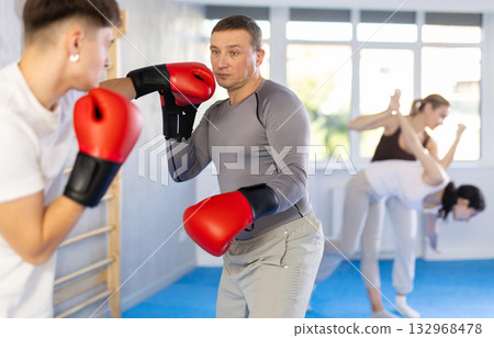 Middle-aged man training boxing with partner during sports classes Middle-aged man training boxing with partner during sports classes 132968478