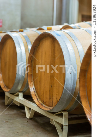 Aging cellar with rows of wine barrels - A view of the winery's storage room Aging cellar with rows of wine barrels - A view of the winery's storage room 132968924