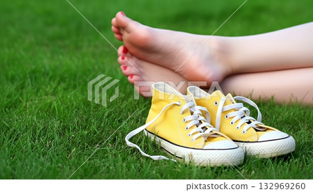 Barefoot person relaxing on green grass with shoes beside 132969260
