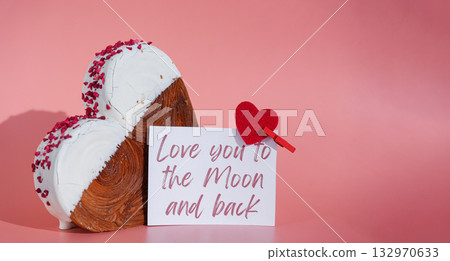 LOVE YOU TO THE MOON AND BACK holiday greeting card Valentine's Day Heart shaped white chocolate croissant on pink background with copy space. Puff pastry new trendy sweet dessert bakery. Creamy dough 132970633